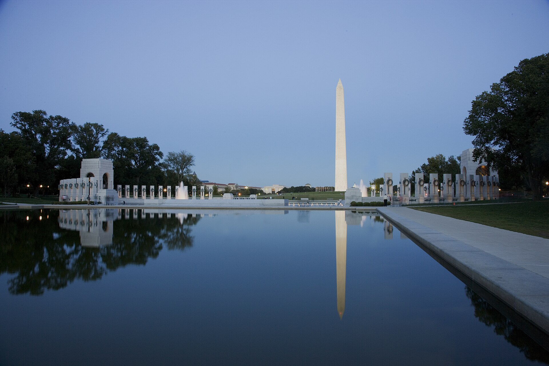 The Washington Monument and memorial fountains reflected in a pool at dusk.